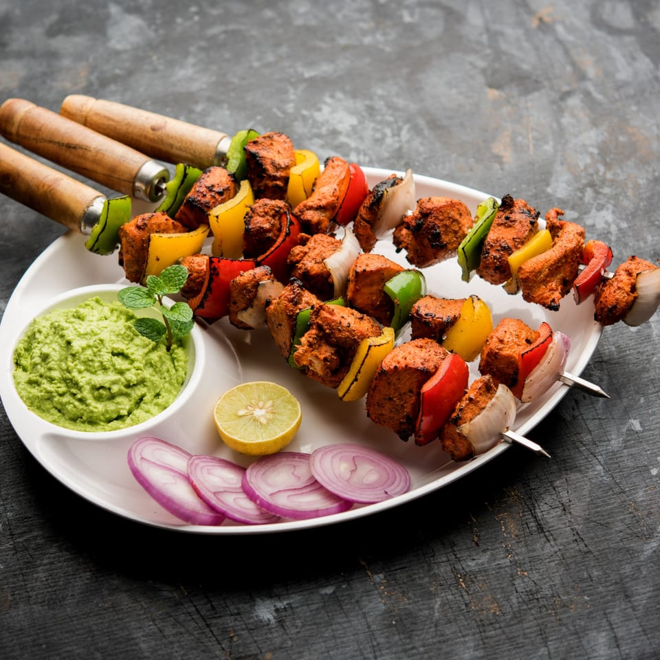 Indian chicken tikka skewers with bell peppers and onions, served with green chutney, lemon, and red onion slices.