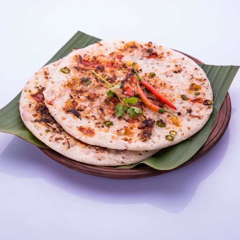 Two Indian Uttapam pancakes with vegetables, chili, and cilantro on a banana leaf.
