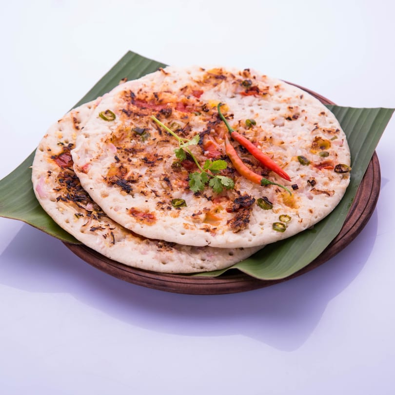 Two Indian Uttapam pancakes with vegetables, chili, and cilantro on a banana leaf.